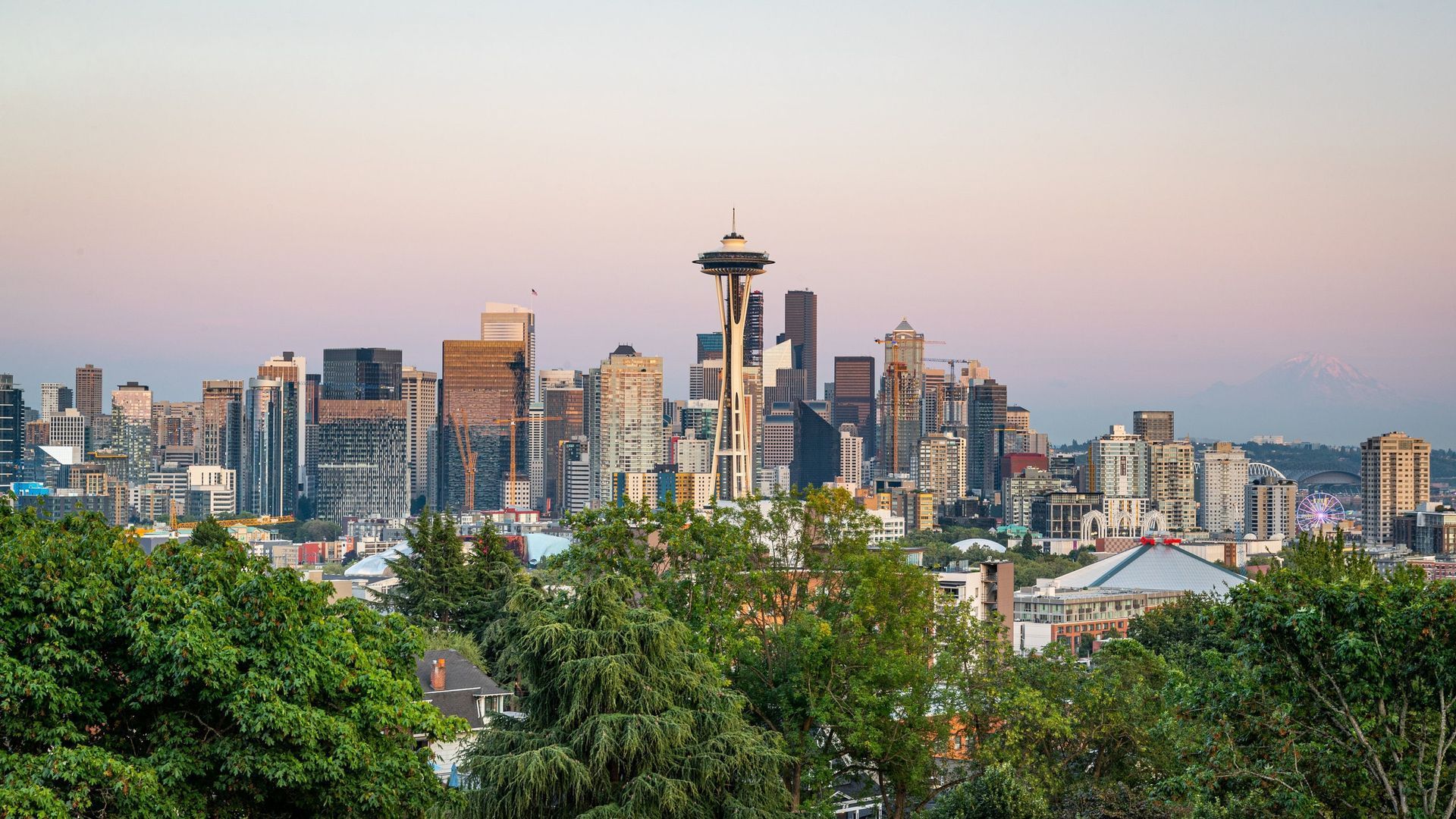 Seattle skyline at dusk with the Space Needle above trees and colorful evening sky