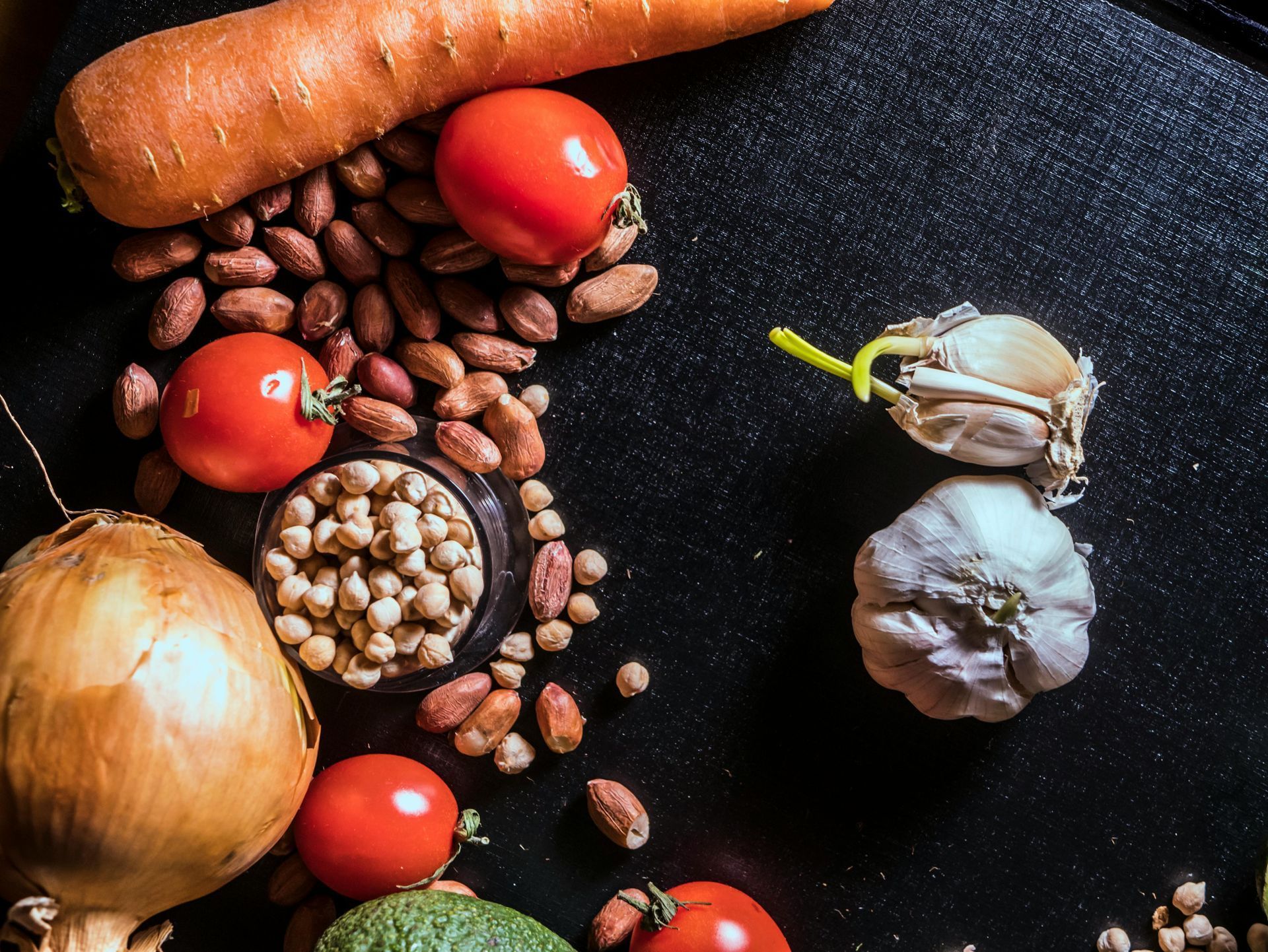 Assorted vegetables, beans, and garlic arranged on a dark surface