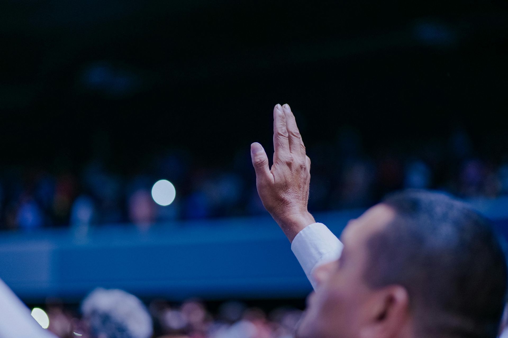 Person raising a hand in a dim auditorium during a public event