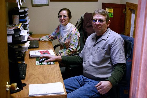 Two people working at a desk. Woman in floral top, man in shirt and sunglasses, both looking forward. Office setting. | Mohr's Automotive
