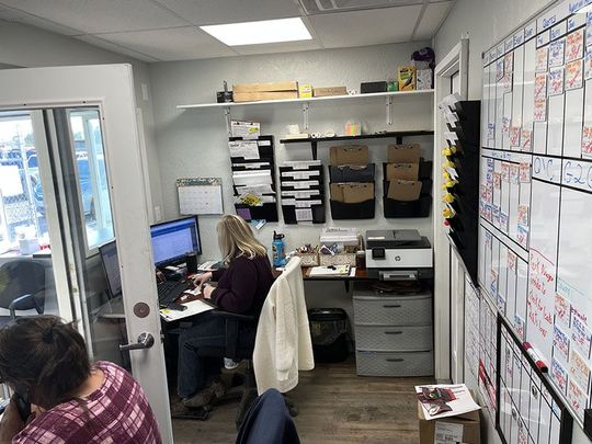 Two people working in a small office with a whiteboard, desk, and computer at Mohr's Automotive | Mohr's Automotive