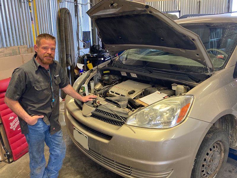Technician standing next to a car with an open hood in a garage. | Mohr's Automotive
