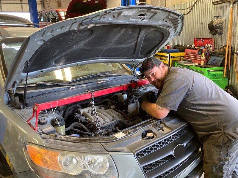 Technician working on car engine, leaning over the open hood in a garage. Red support bar in place. | Mohr's Automotive