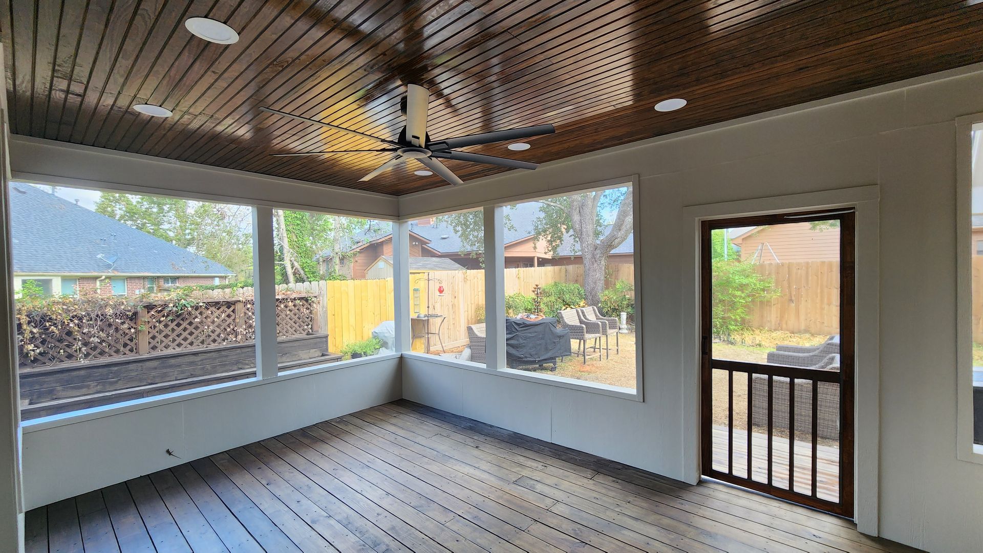 Covered porch with wooden ceiling, white walls, large windows, and a door opening to a backyard.