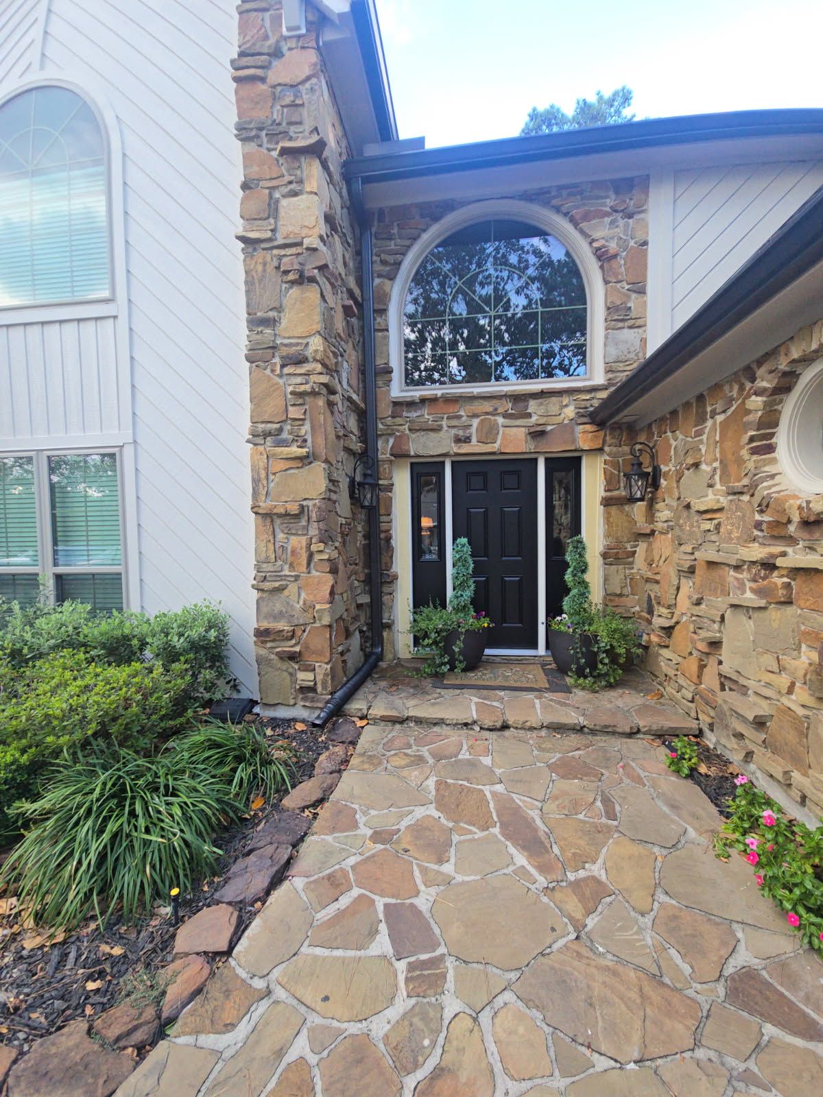 Stone entryway and front door of a house with arched window and flagstone walkway