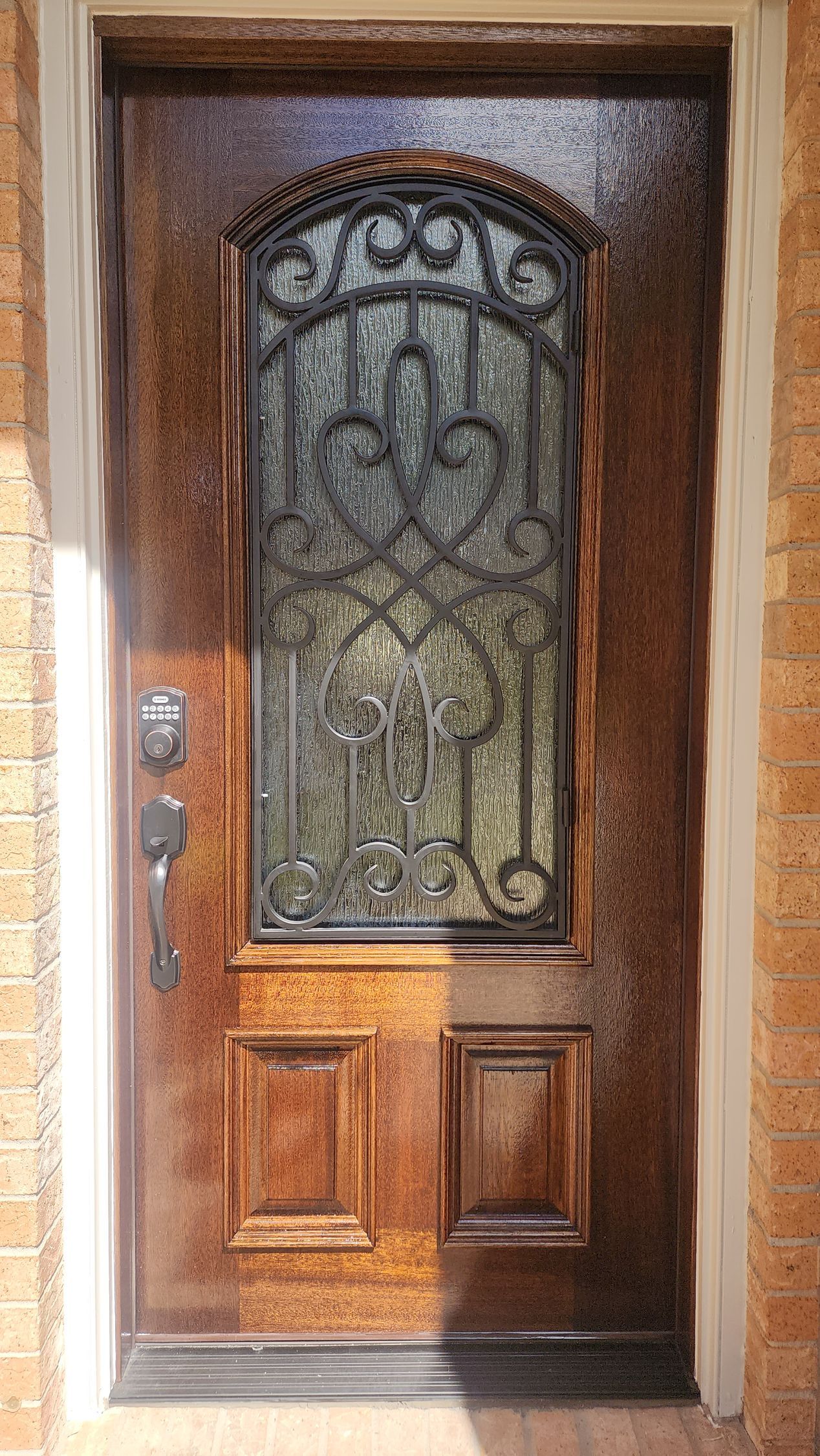 Wooden front door with decorative wrought-iron glass panel and silver handle in a stucco entryway