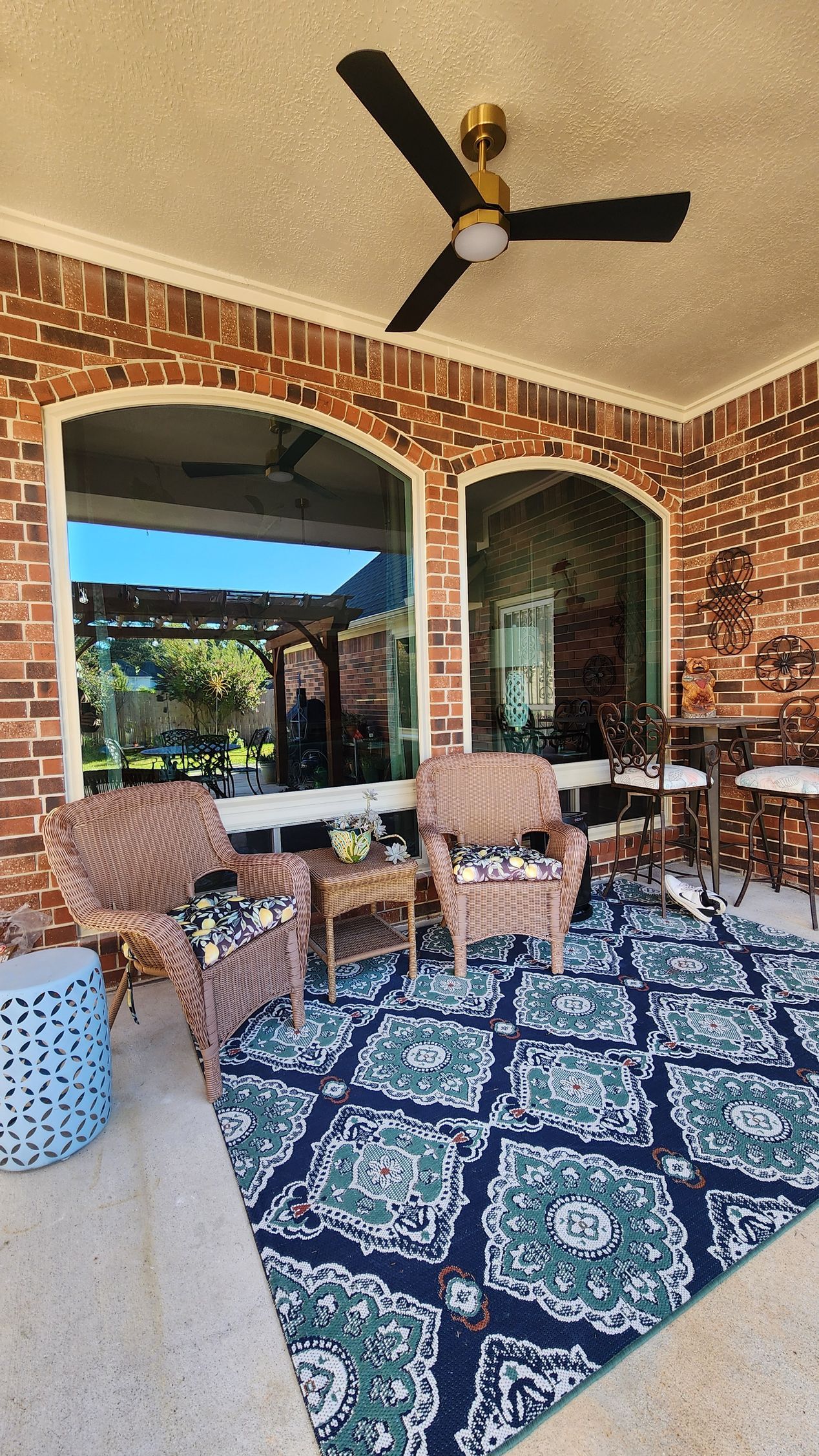 Covered patio with brick arches, patterned blue rug, wicker chairs, and a ceiling fan overlooking a scenic view