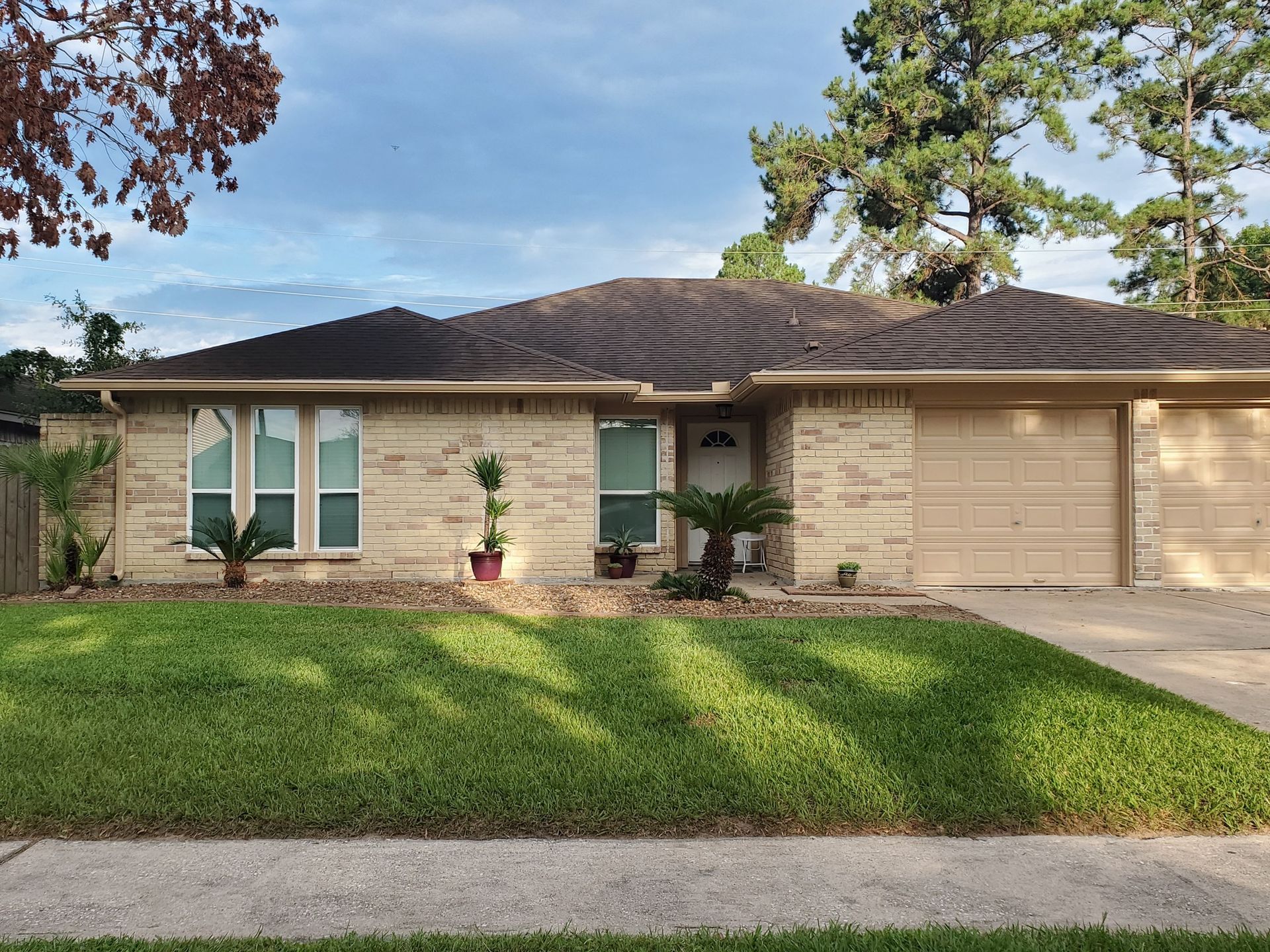 Single-story brick house with a front lawn, driveway, and attached garage under a partly cloudy sky