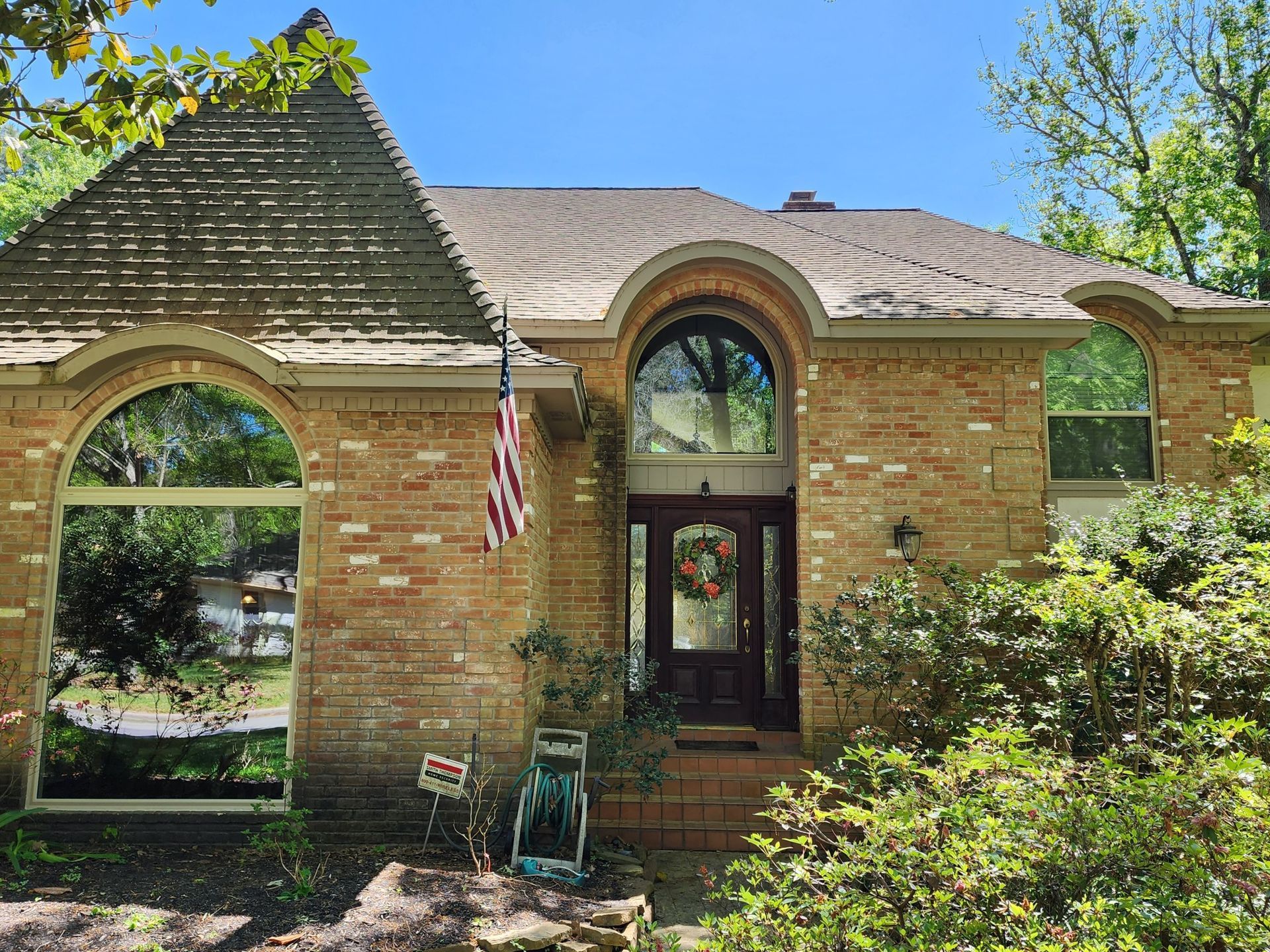Brick house with arched windows, front door, and an American flag in a sunny yard.