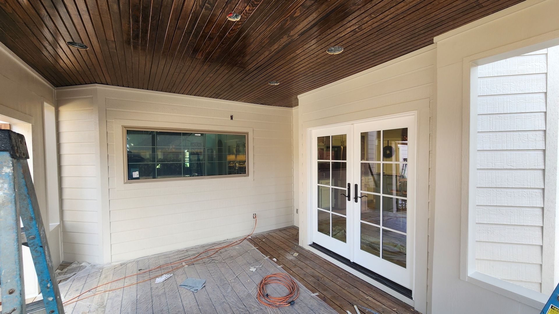 Covered patio with white walls, wood ceiling, French doors, window, and tiled floor