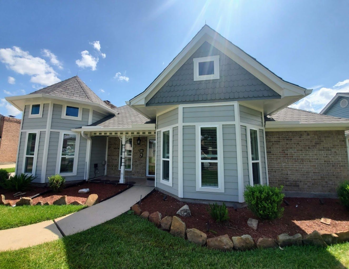 Front view of a gray and white suburban house with a brick exterior, arched walkway, and landscaped yard