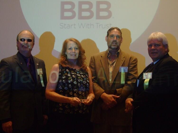 Four people posing at a BBB event in front of a BBB logo backdrop