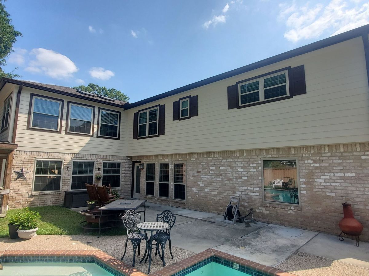 Courtyard patio beside a two-story home with stone and cream siding, table, chairs, and potted decor