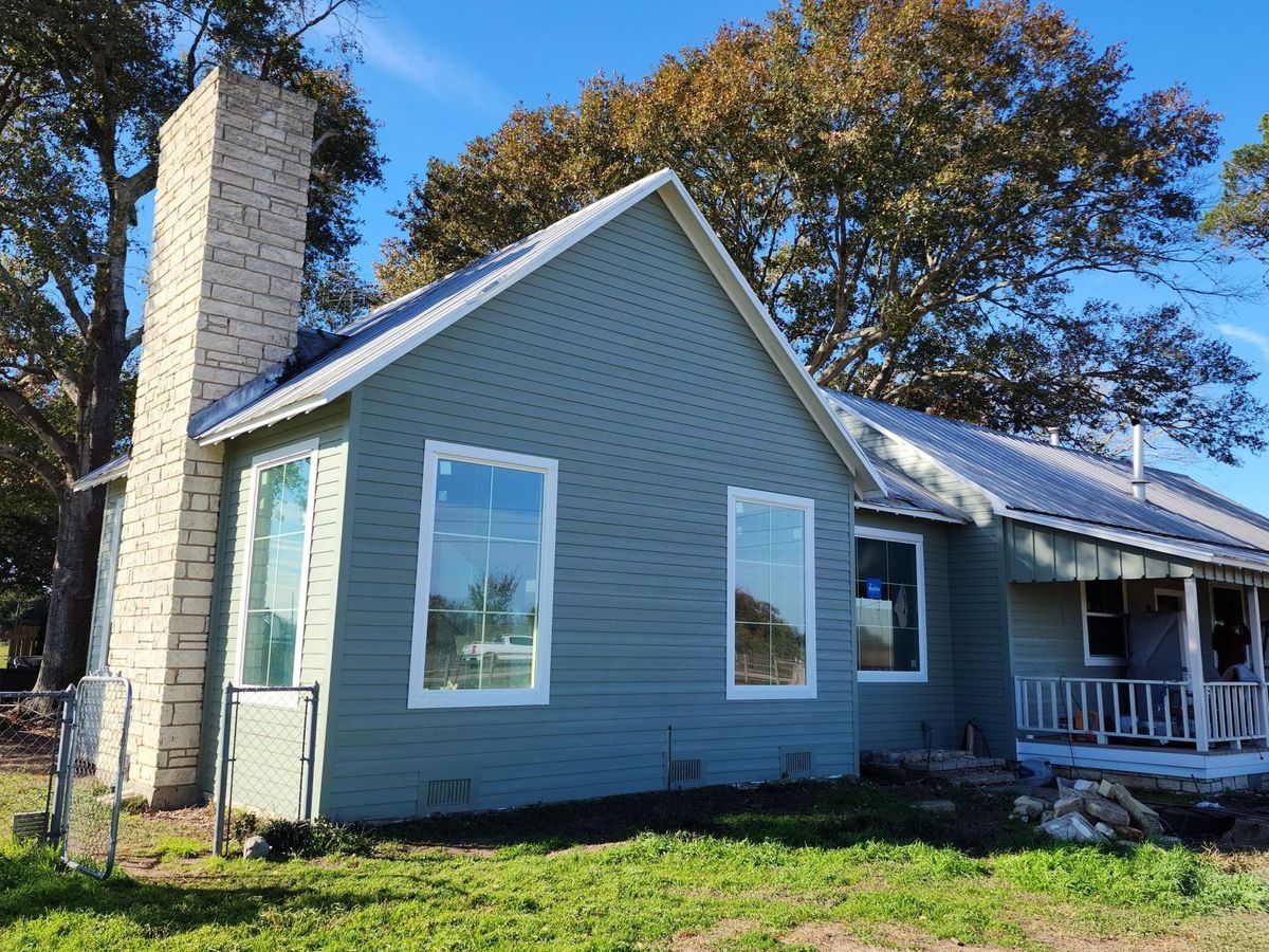 Gray house with stone chimney and white porch in a sunny yard