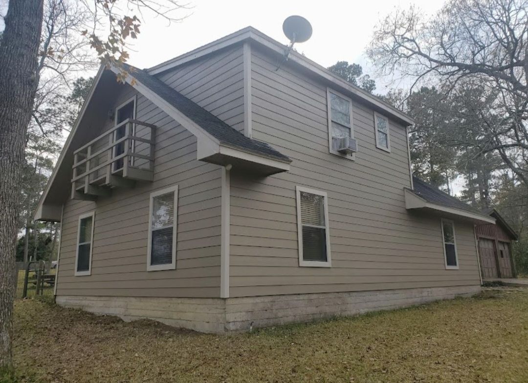 Beige two-story house with a small balcony, satellite dish, and bare trees in a yard