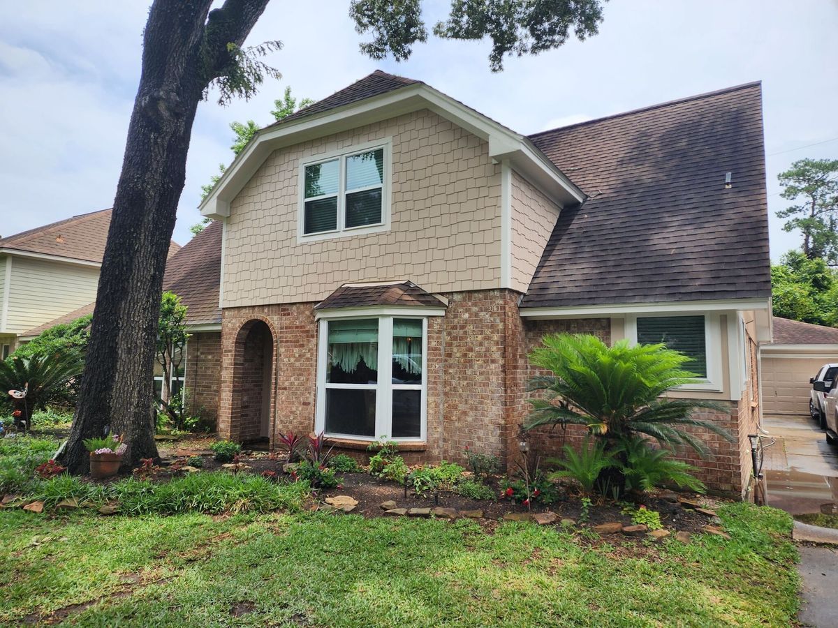 Two-story brick and beige house with a front lawn, large window, and tall tree in the yard