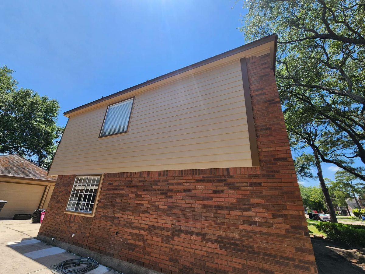 Brick-and-beige two-story house exterior under a blue sky, viewed from the side