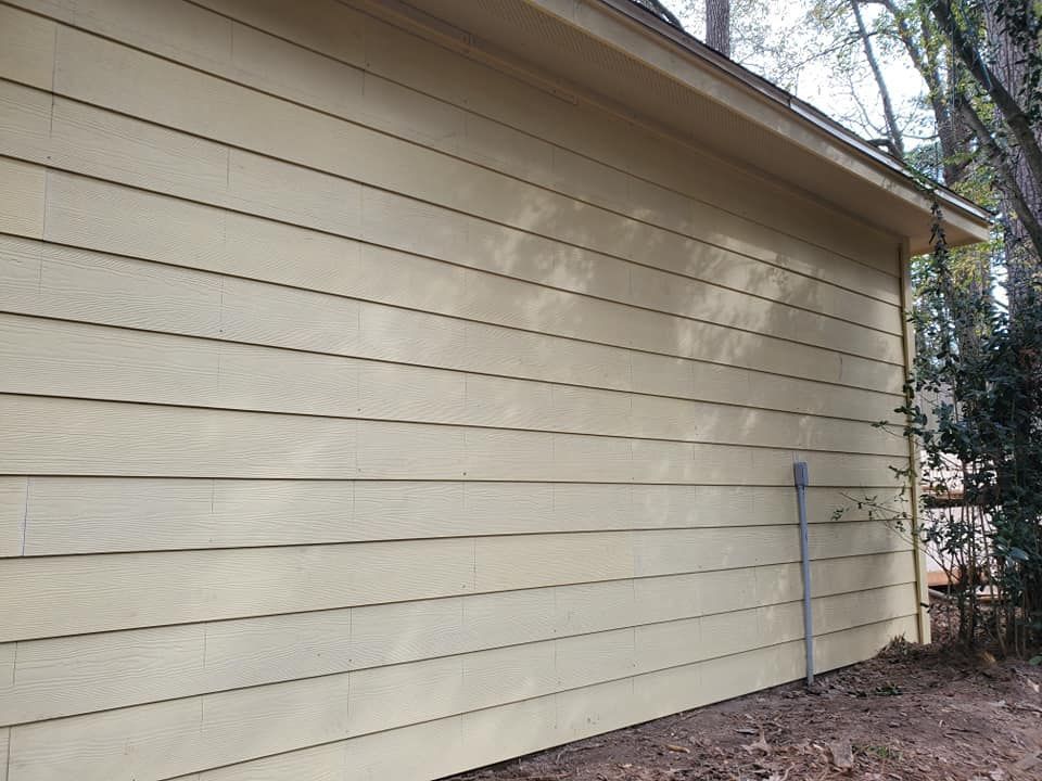 Side of a beige house with horizontal siding and a blue pole near a wooded yard