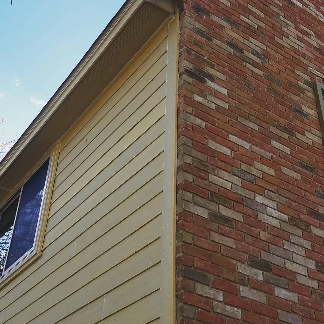 Corner of a house with beige siding and red brick exterior under a blue sky