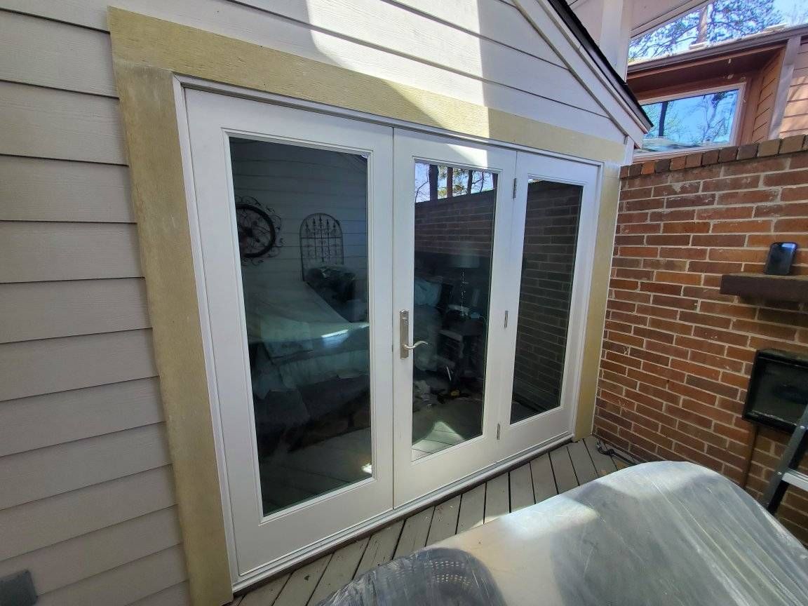 White French doors on a beige house exterior beside a brick patio and covered grill.