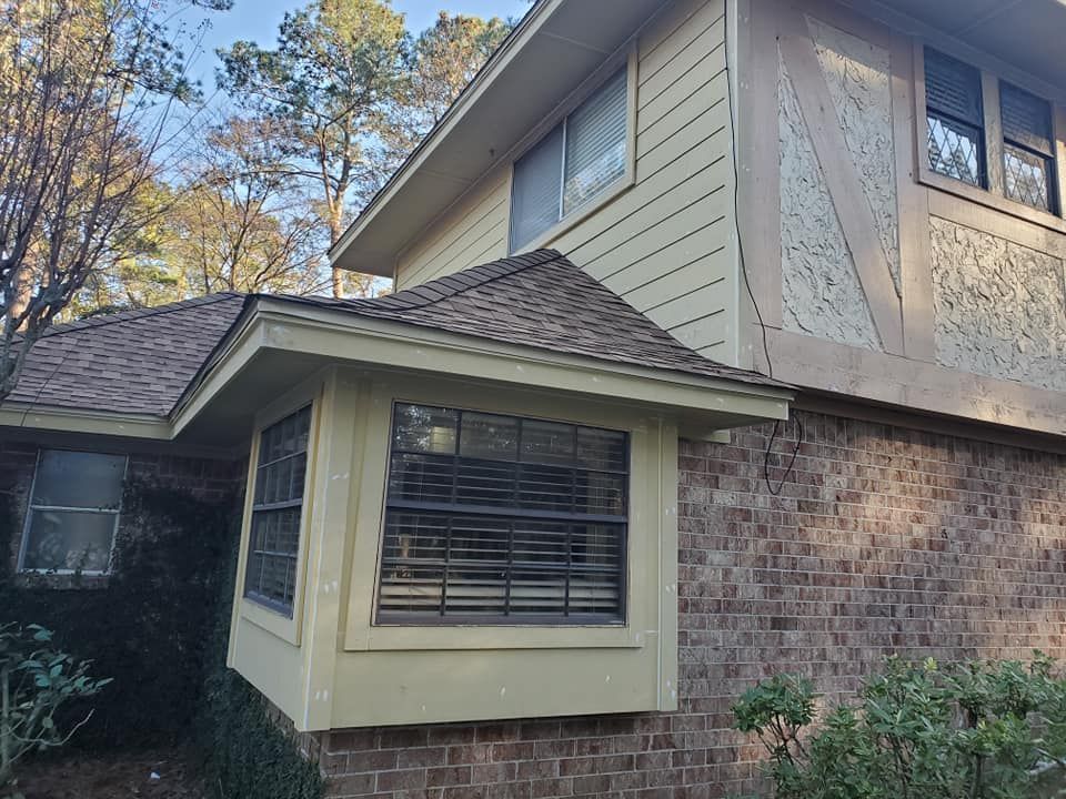 Suburban house exterior with beige siding, brick walls, and a bay window under a shingled roof.