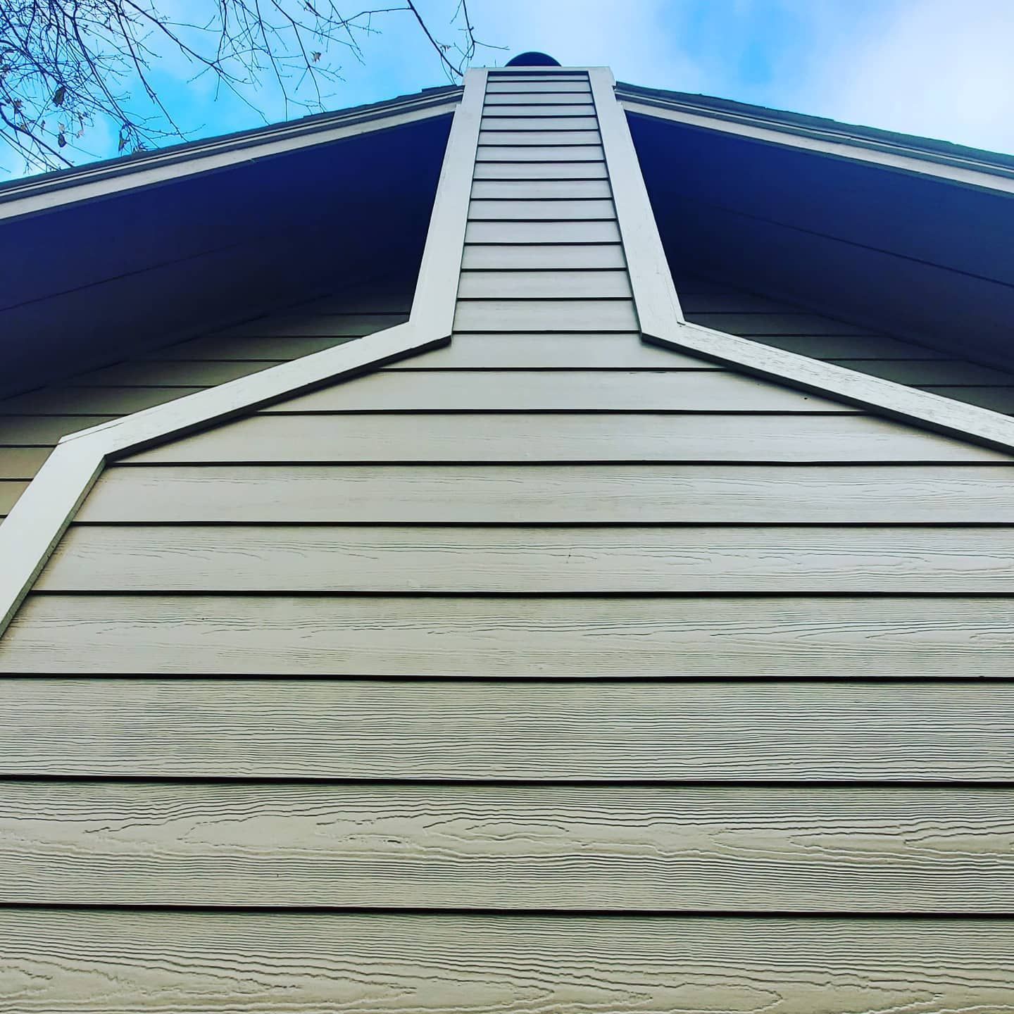 Close-up of a house gable with weathered gray siding and white trim against a blue sky.