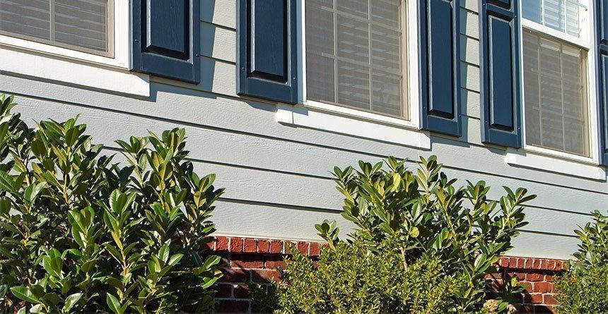 House exterior with gray siding, blue shutters, and leafy green shrubs in front.