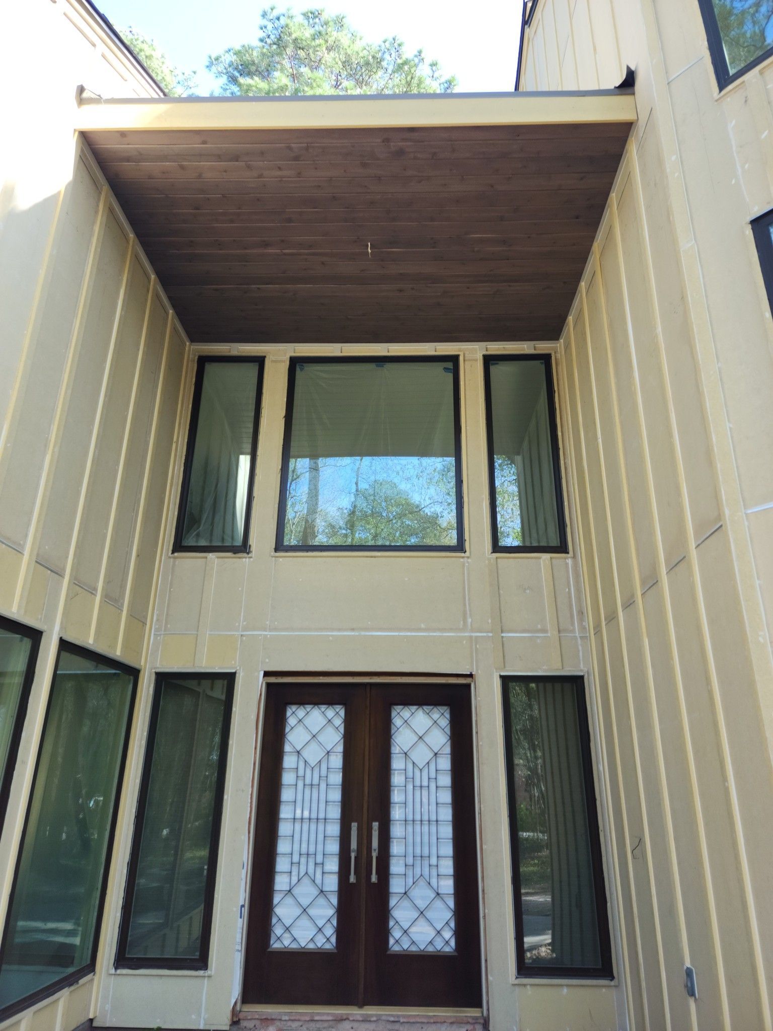Modern house entrance with double wooden doors, tall windows, and a covered overhang