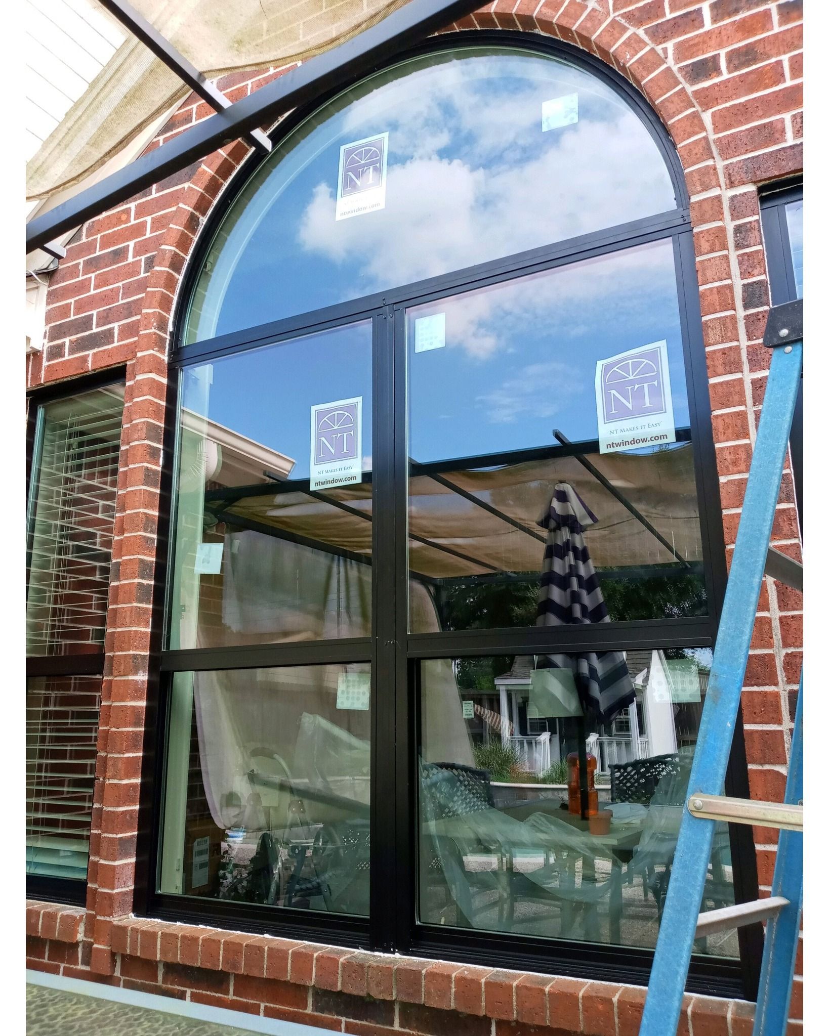 Arched brick storefront window with reflective glass and a blue ladder leaning beside it