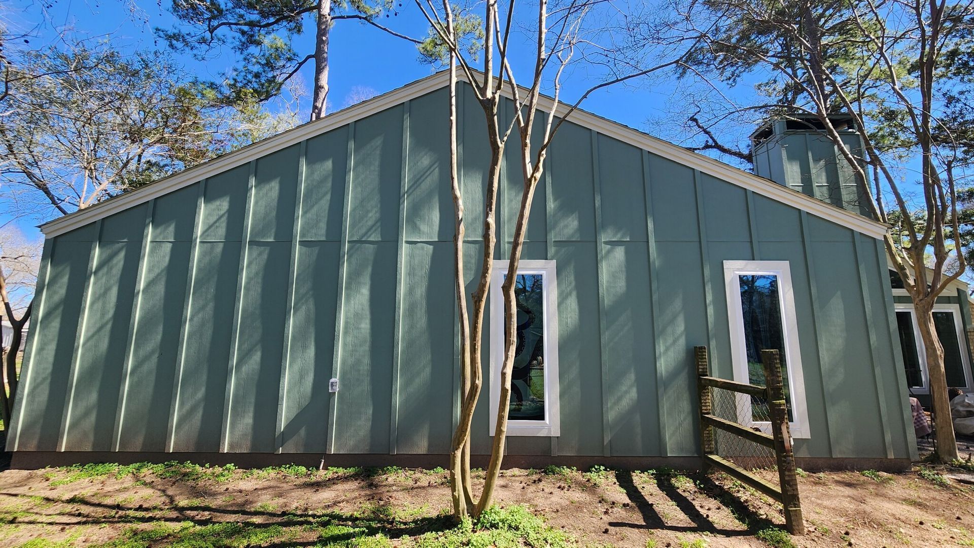 Green cabin-style building with white-trimmed windows and a gabled roof among trees.