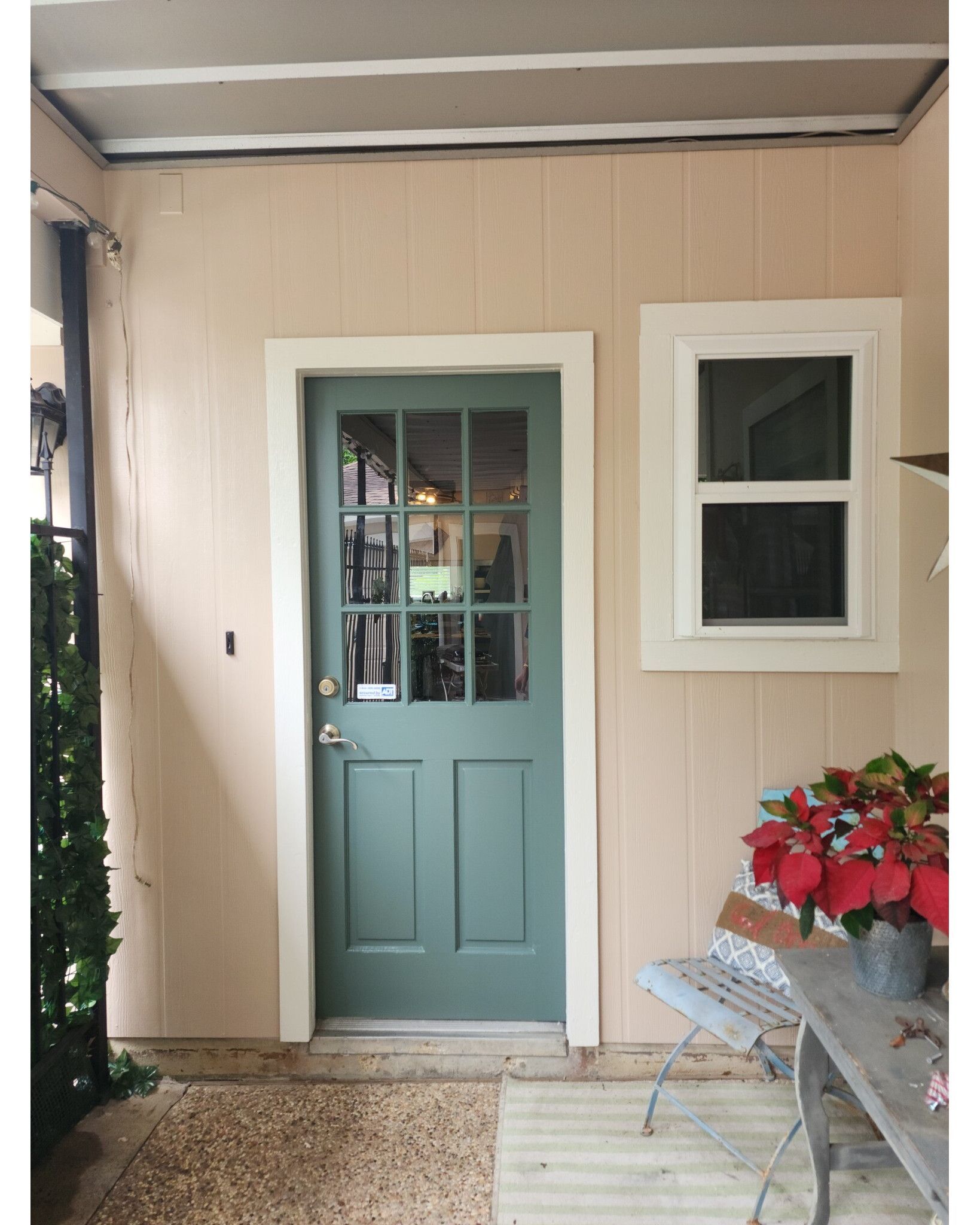 Front porch with a mint-green door, white-framed window, bench, and red potted flowers.