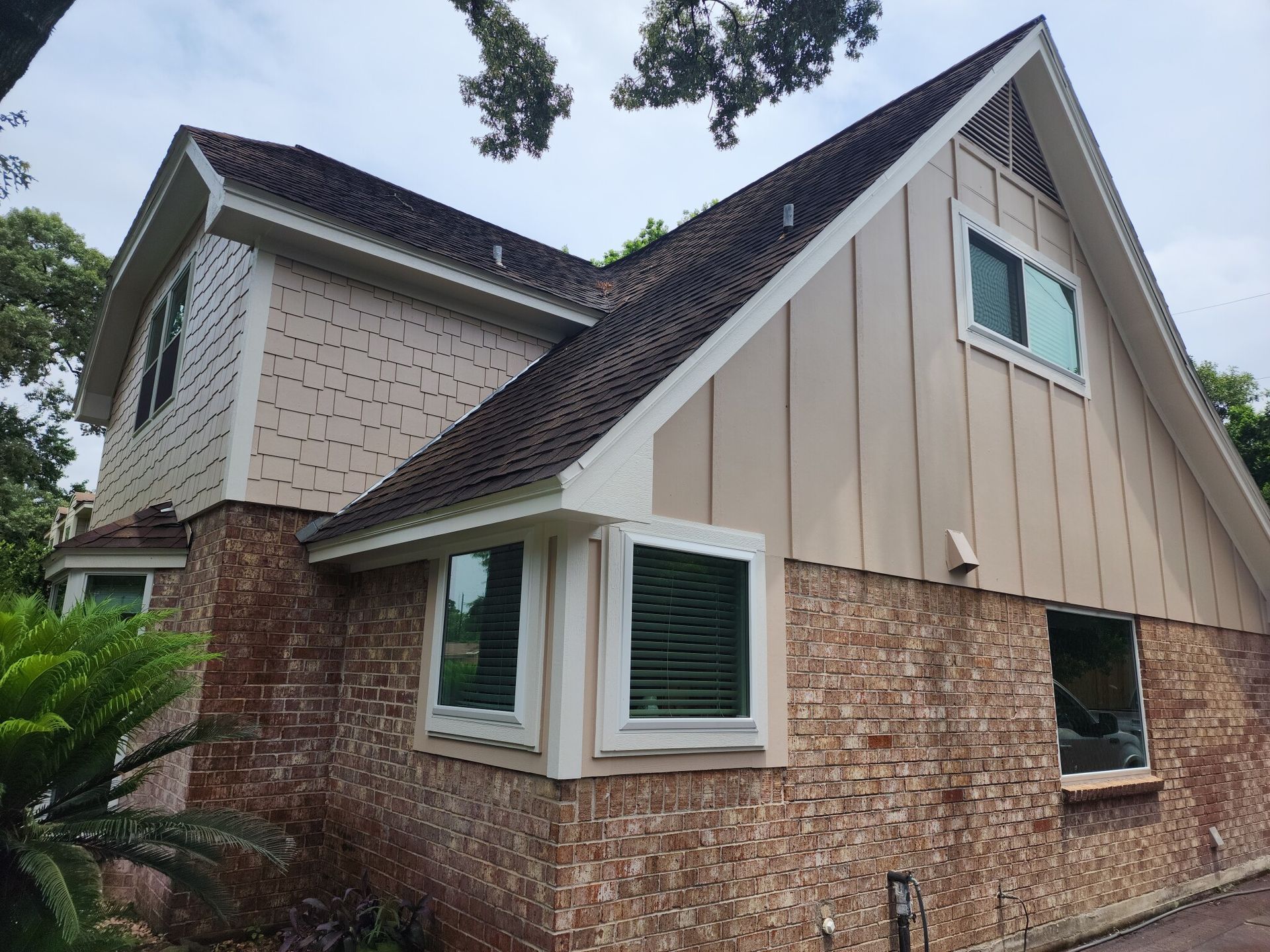 Exterior of a two-story house with brick, tan siding, and a steep dark roof under cloudy skies