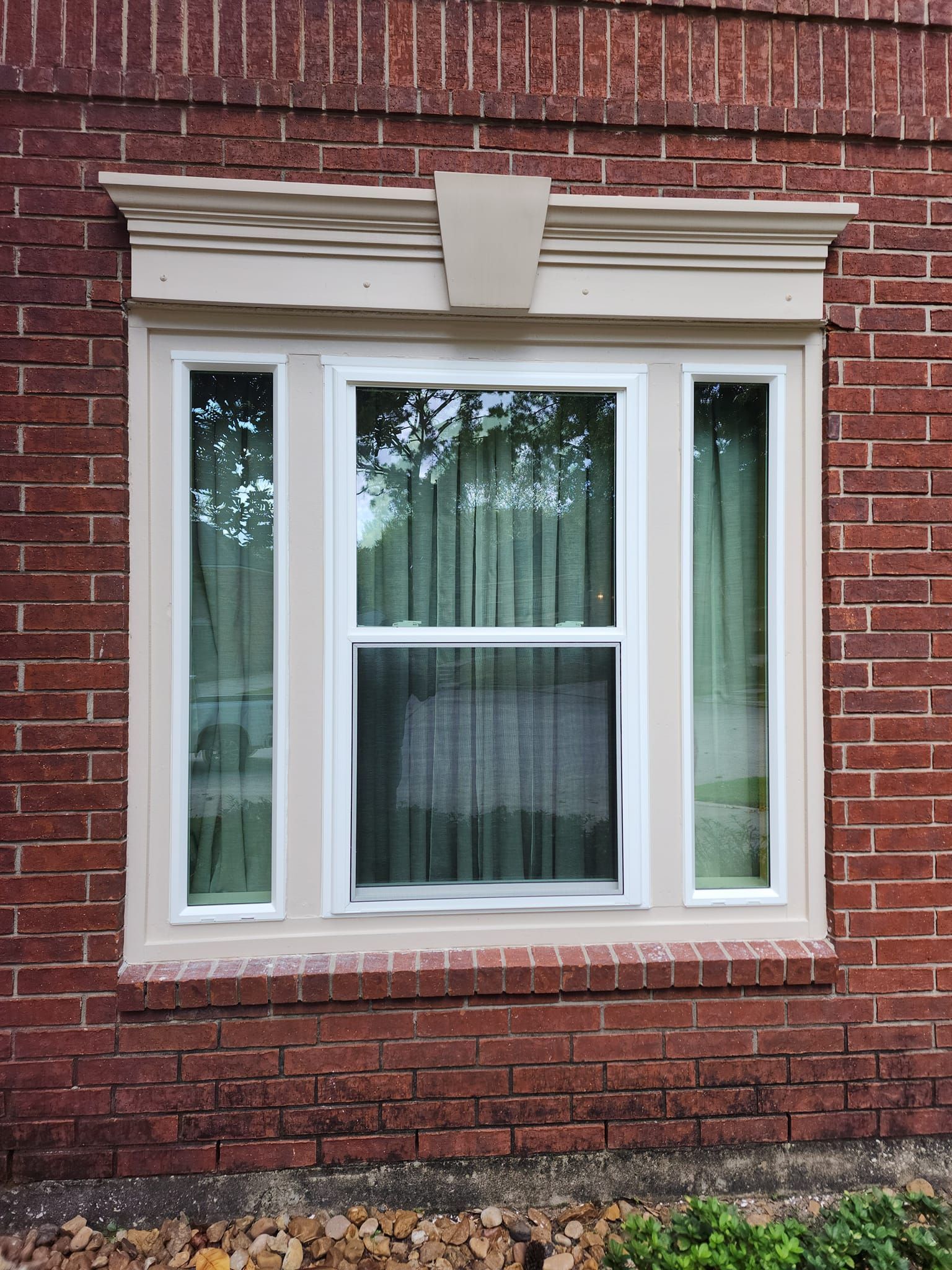 White-trimmed bay window set in a red brick wall with cream decorative molding above.