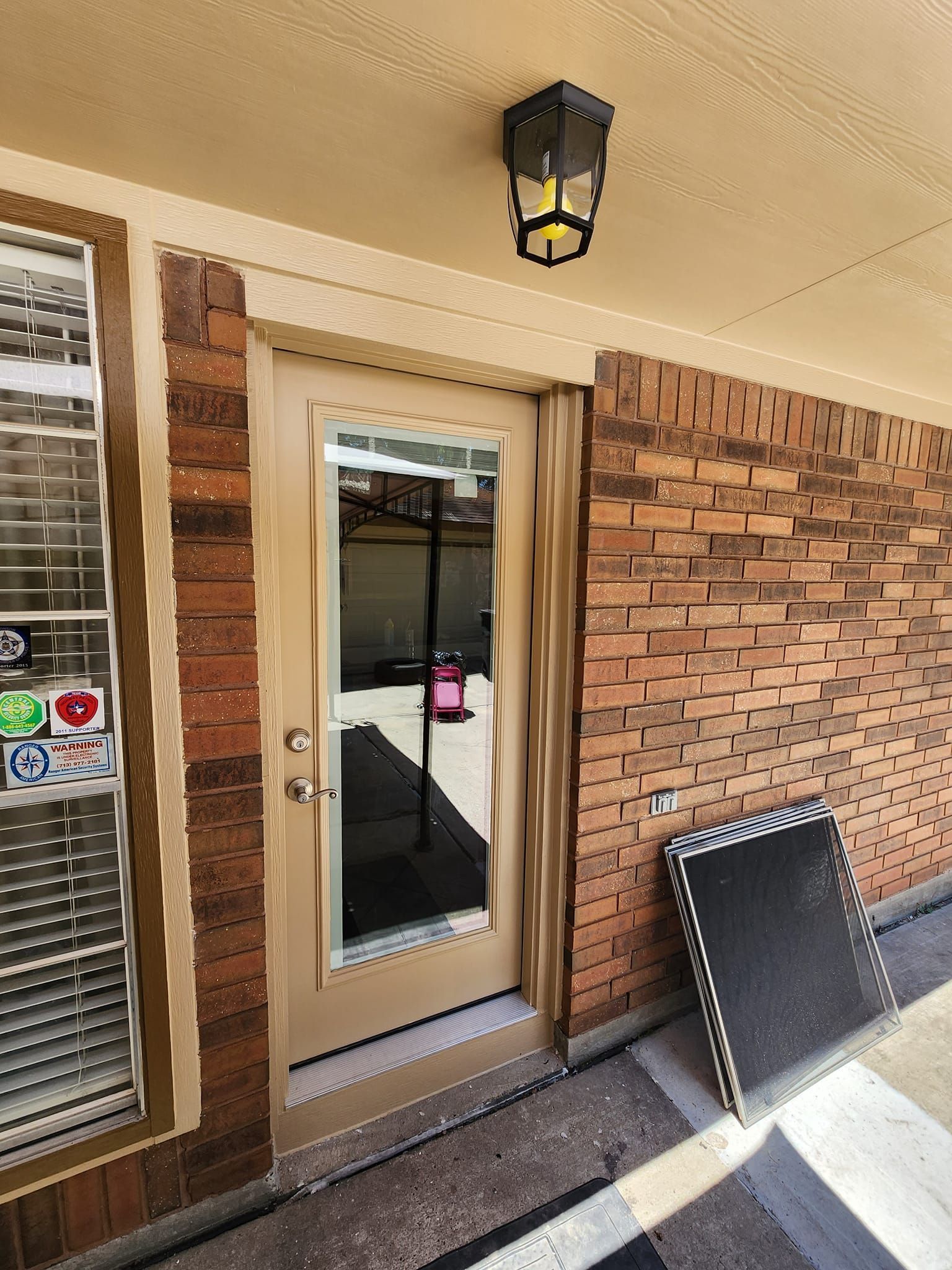 Front entrance with beige door, brick walls, wall light, and a chair by the porch.