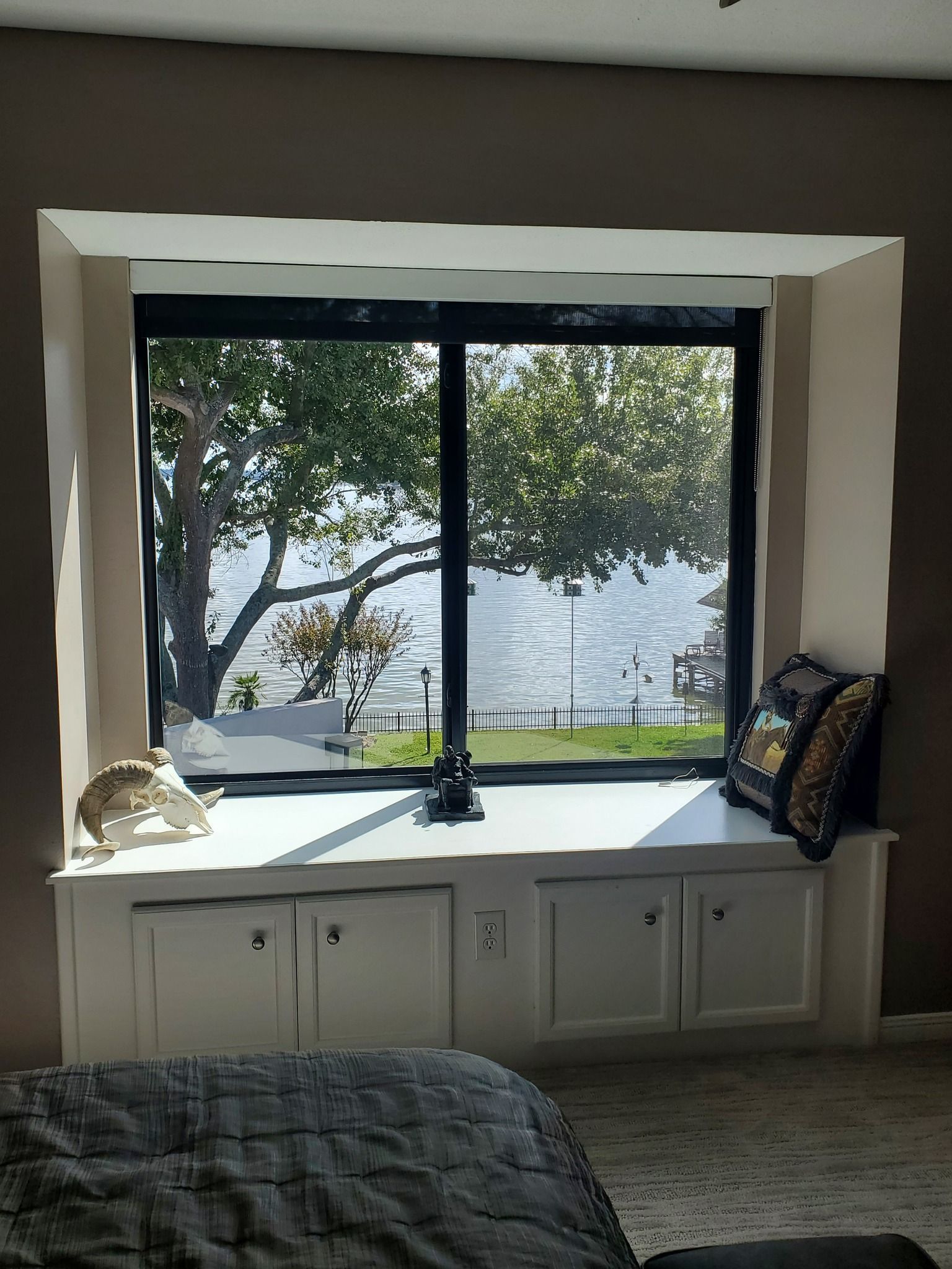 Cozy bedroom window seat with white cabinets, cushions, and a tree-filled view outside