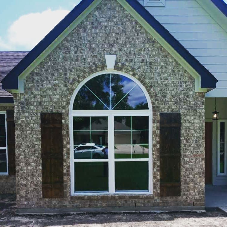 Front of a brick house with a large arched window and white siding gable