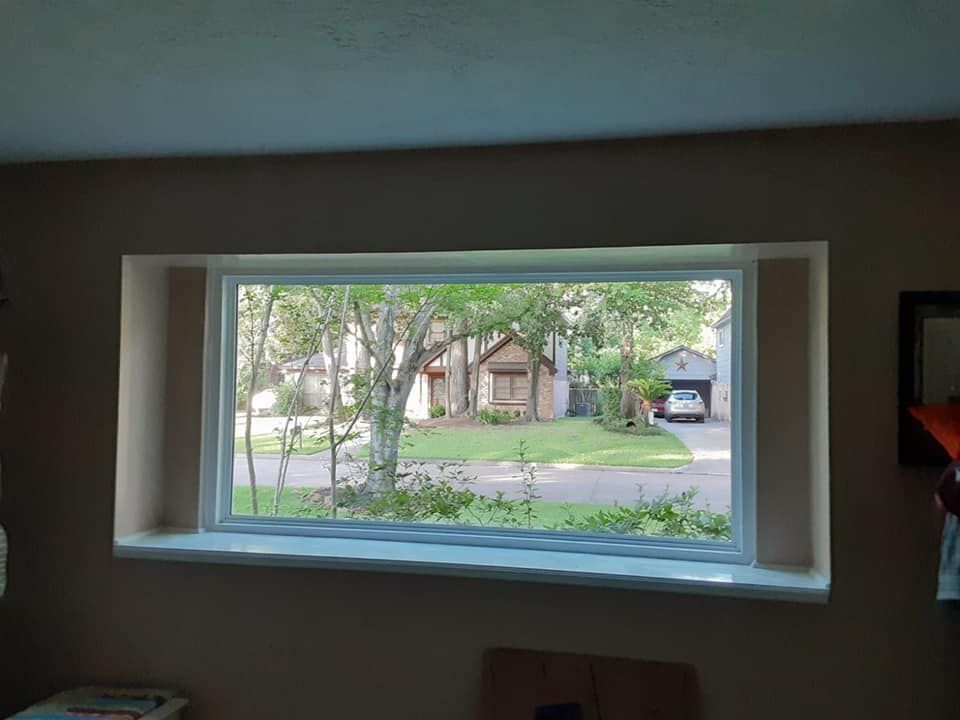 View through a living room window of a tree-lined suburban street and house across the road
