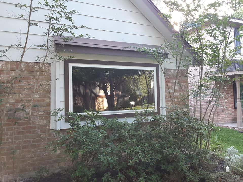 House exterior with white siding, brick wall, large window, and shrubs in front