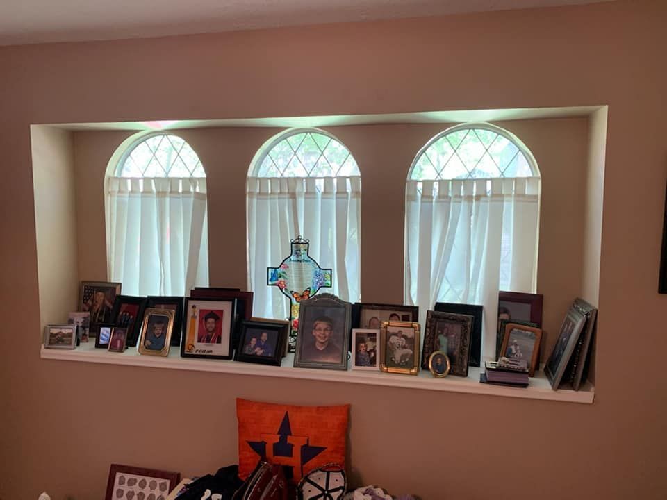 Framed family photos and candles displayed on a shelf beneath three arched windows in a beige room