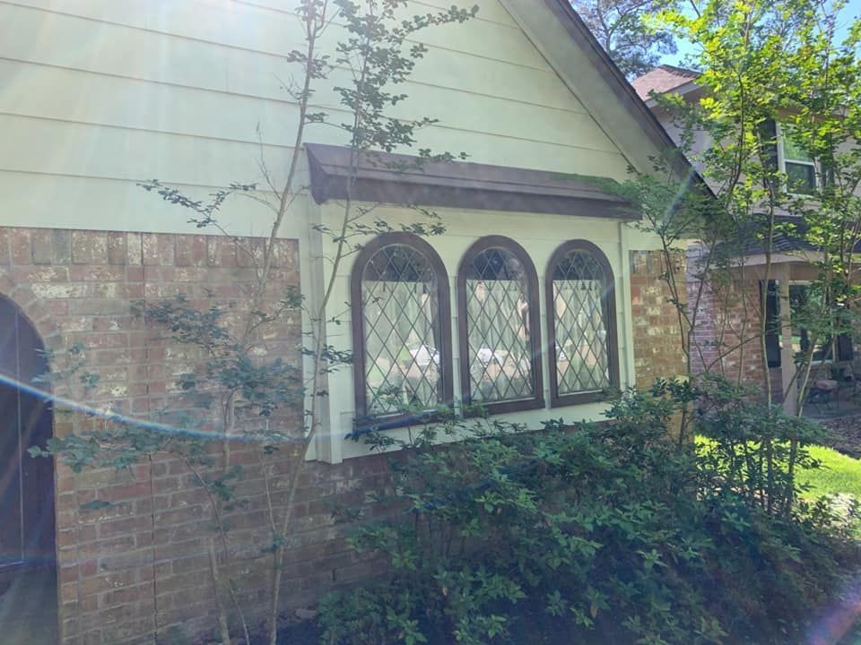 Brick house exterior with arched windows, pale siding, and overgrown shrubs in front