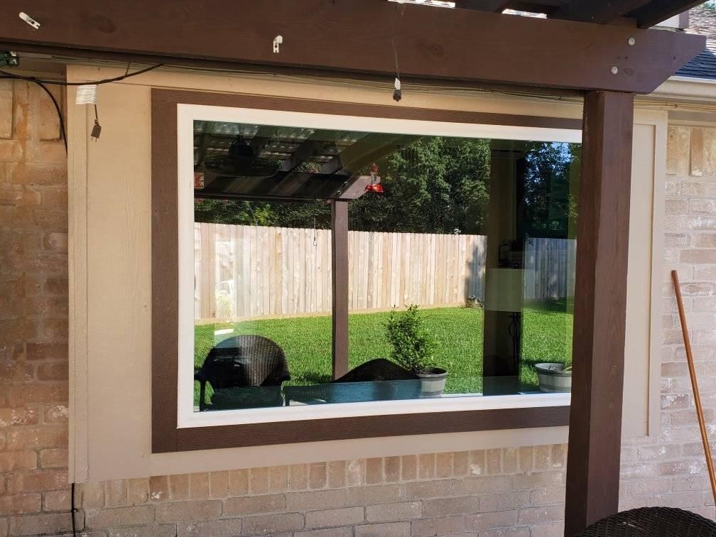 Covered patio with a large window opening to a backyard and wooden fence.