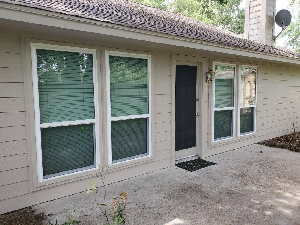 Exterior of a beige house with large windows, a black front door, and a concrete patio.