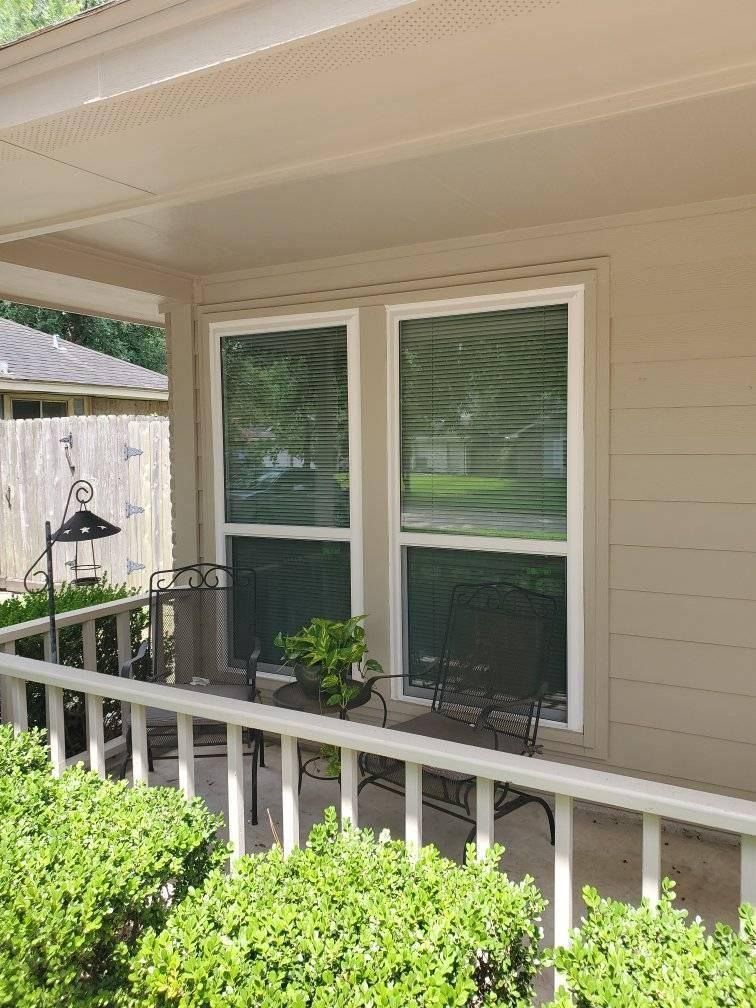 Covered front porch with beige siding, white railing, and a window overlooking a green yard