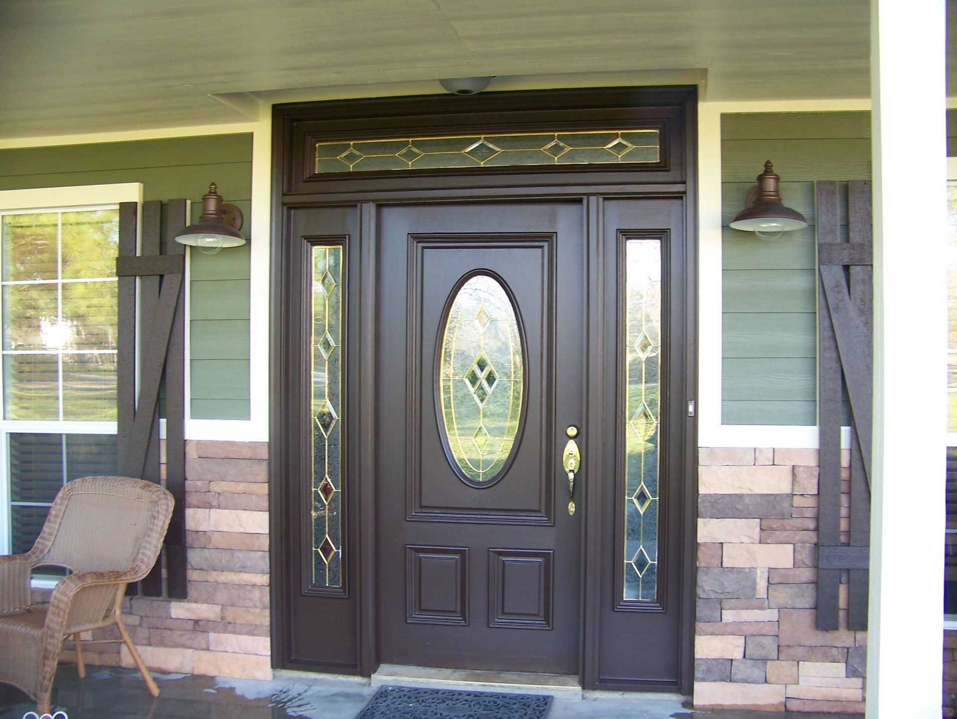 Front porch with a dark double door, oval glass inset, hanging lanterns, and a chair on the left.