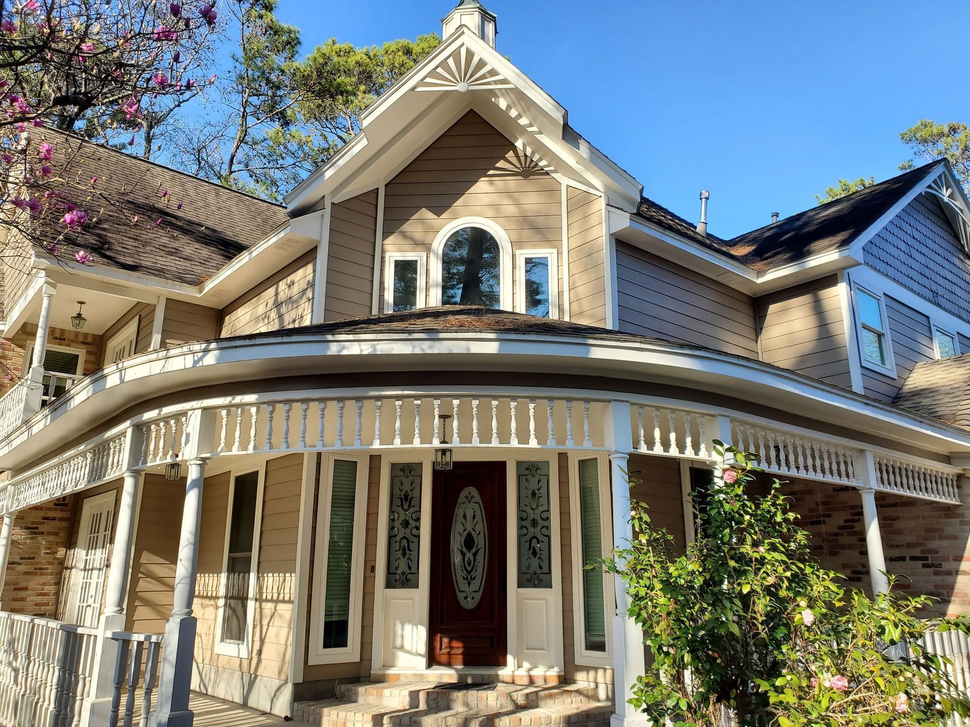 Victorian-style house with a wraparound porch, cream siding, and ornate trim in bright sunlight