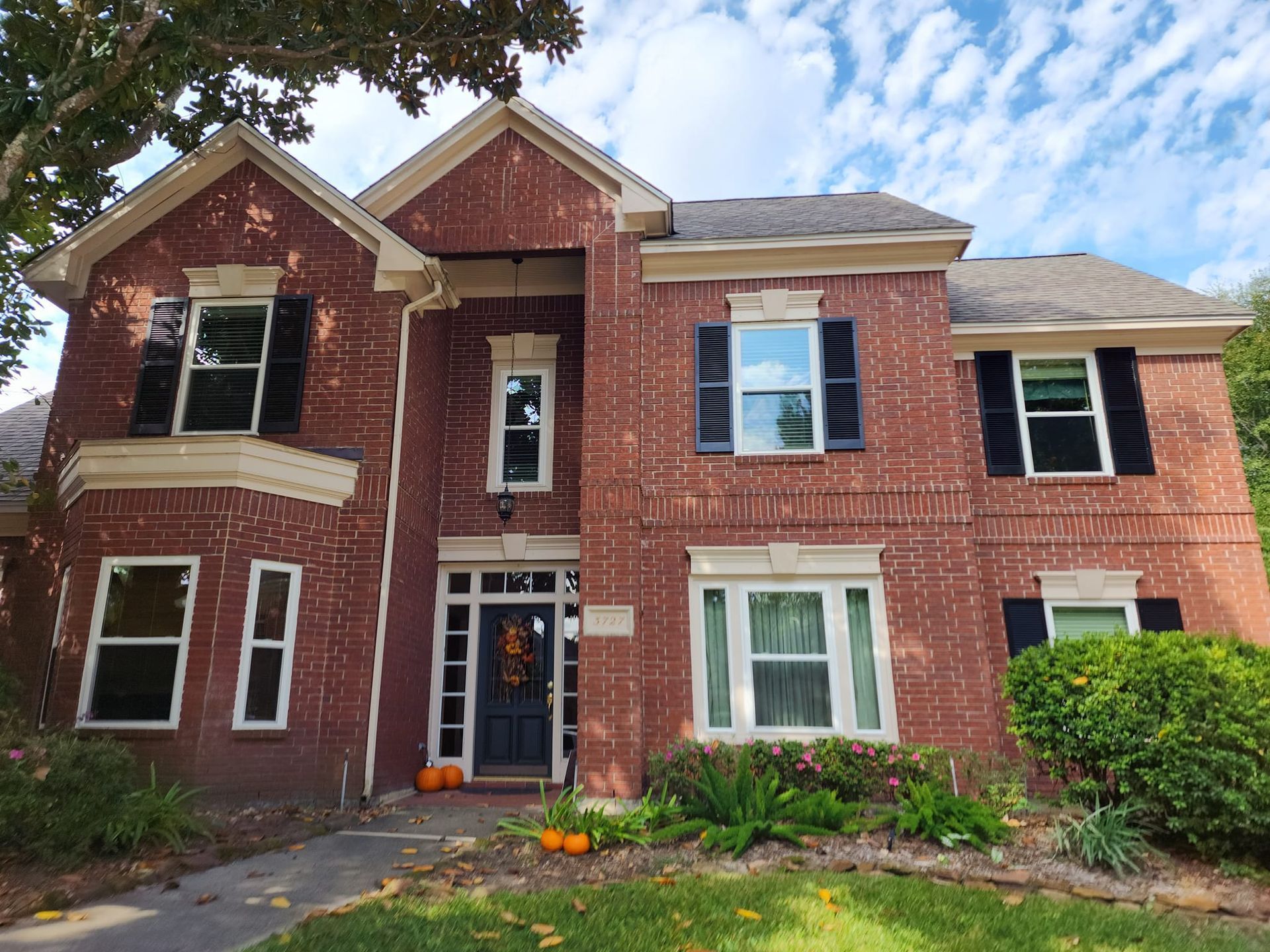 Brick two-story house with black shutters, white trim, and a front walkway under a partly cloudy sky