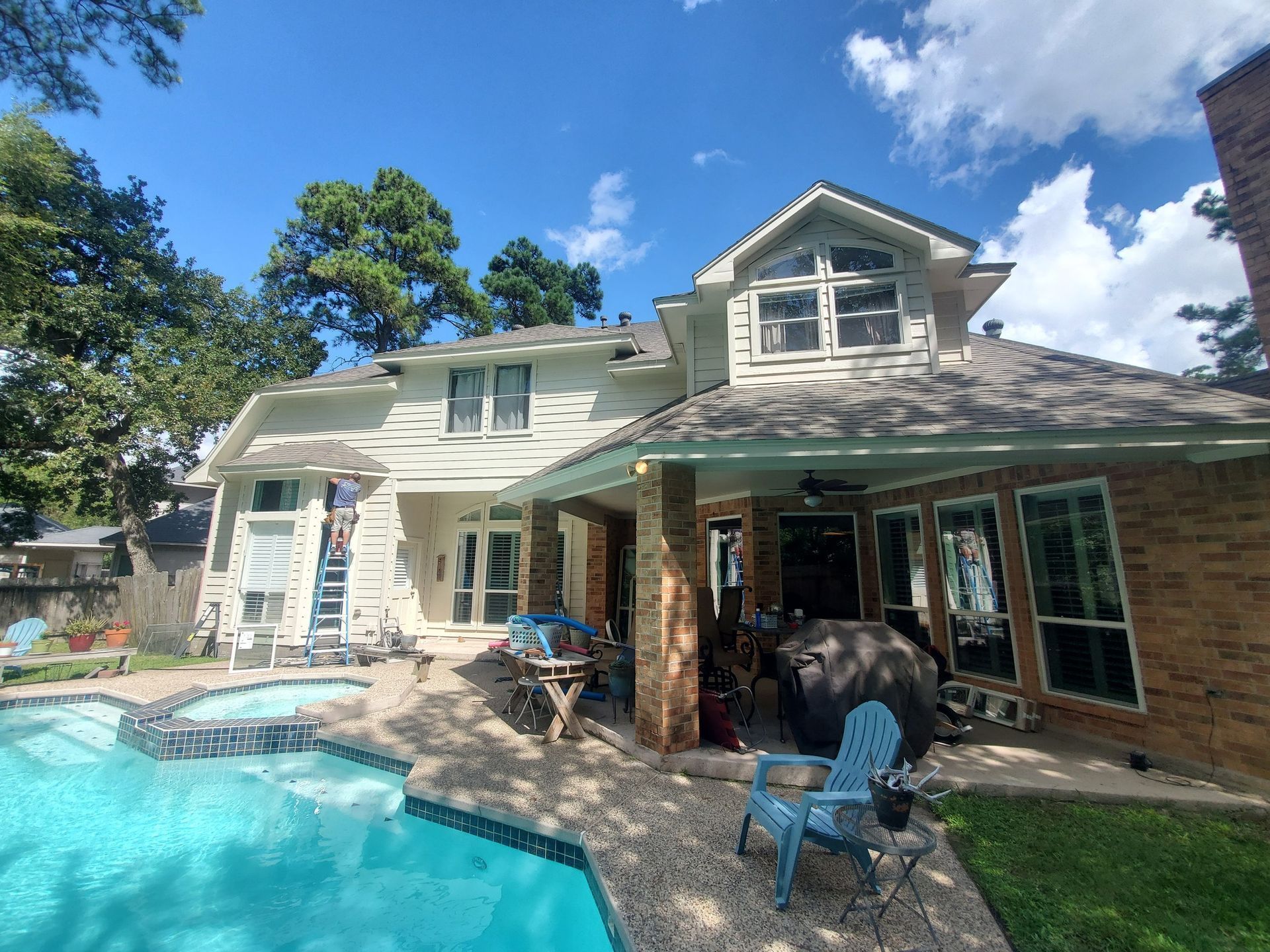 Backyard pool beside a white house with a covered patio and blue sky overhead