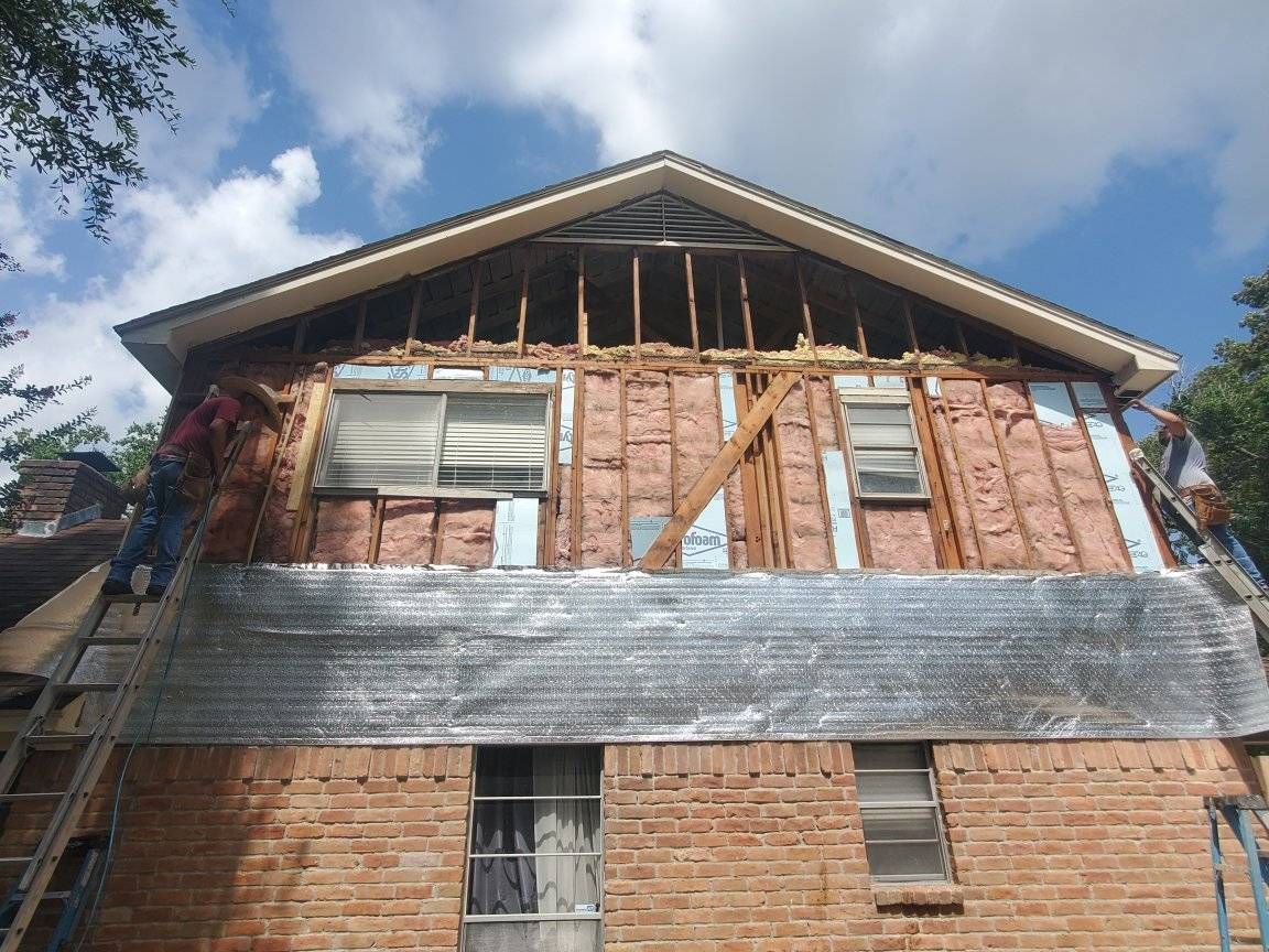 Damaged brick house with exposed framing and roof under repair against a blue sky