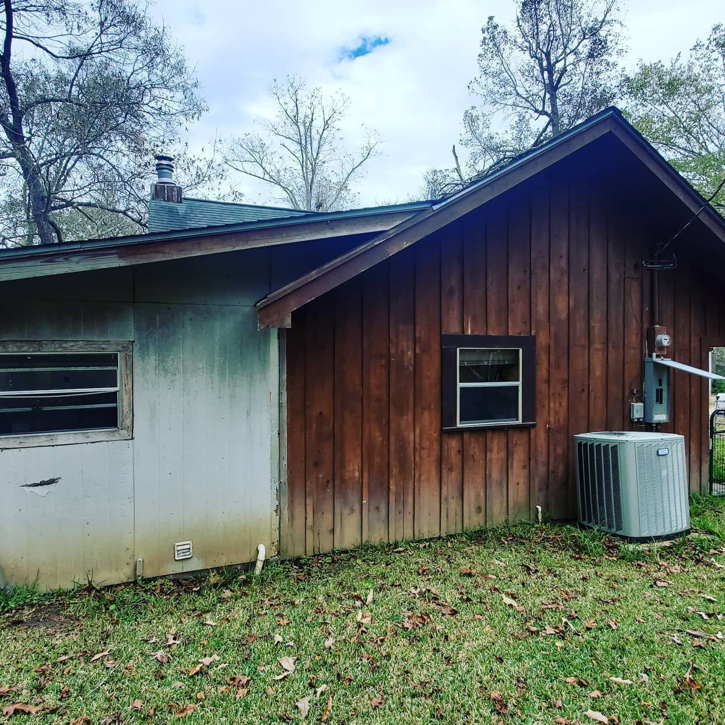 Weathered wooden shed with white siding, small windows, and an air conditioner in a grassy yard.