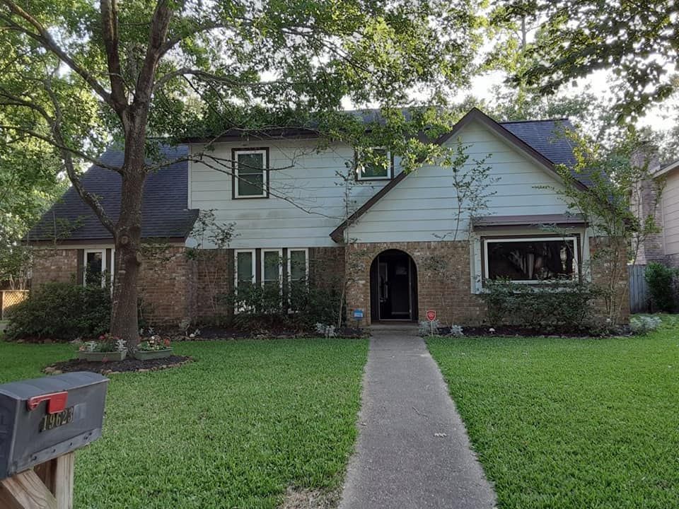 Suburban house with brick and white siding, centered walkway, and large trees in front yard